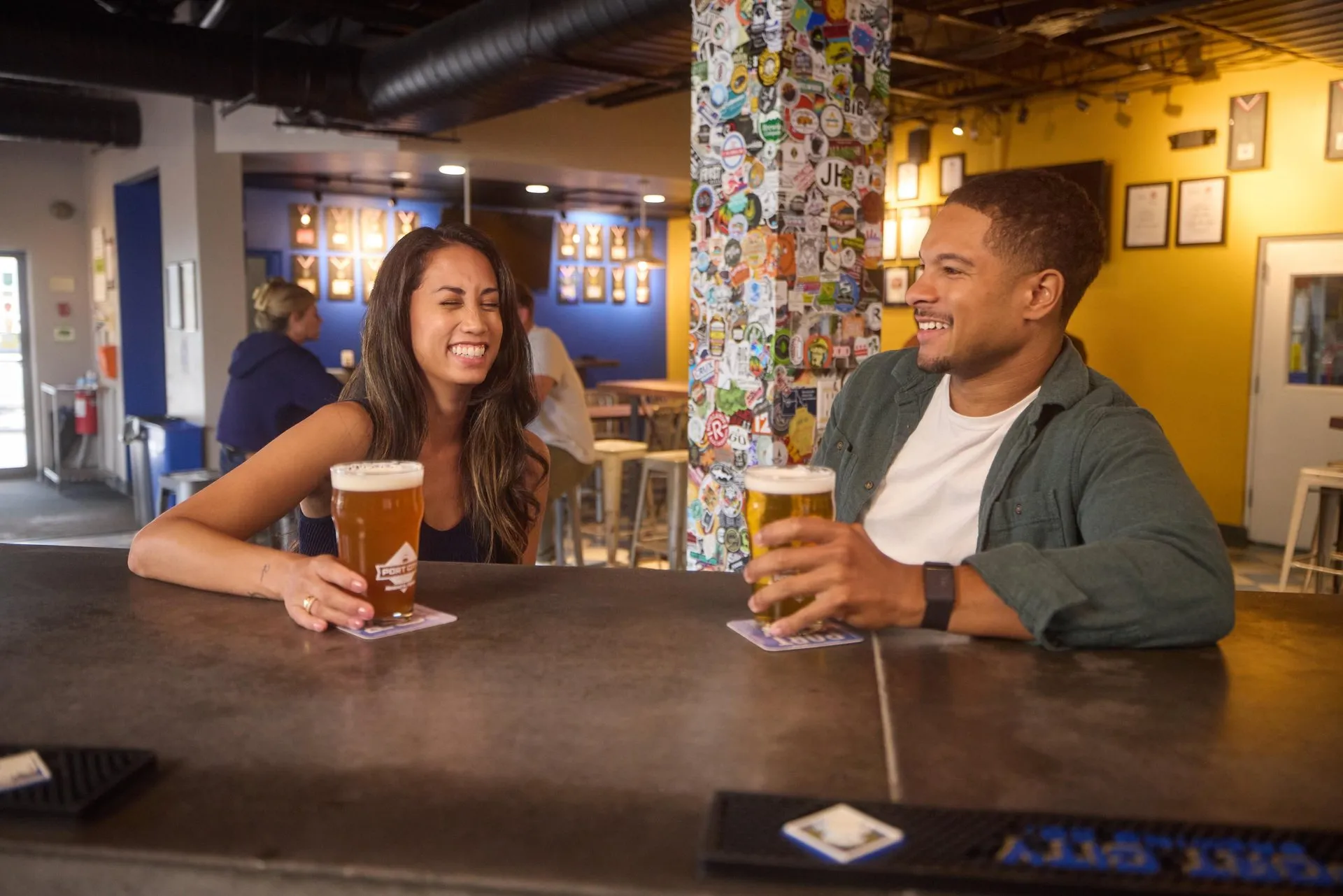 A man and woman laugh and drink beers while sitting at the bar at Port City Brewing Company in Alexandria, VA.
