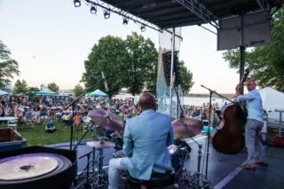 A jazz band performs on an outdoor stage for a large crowd at an Alexandria summer festival.