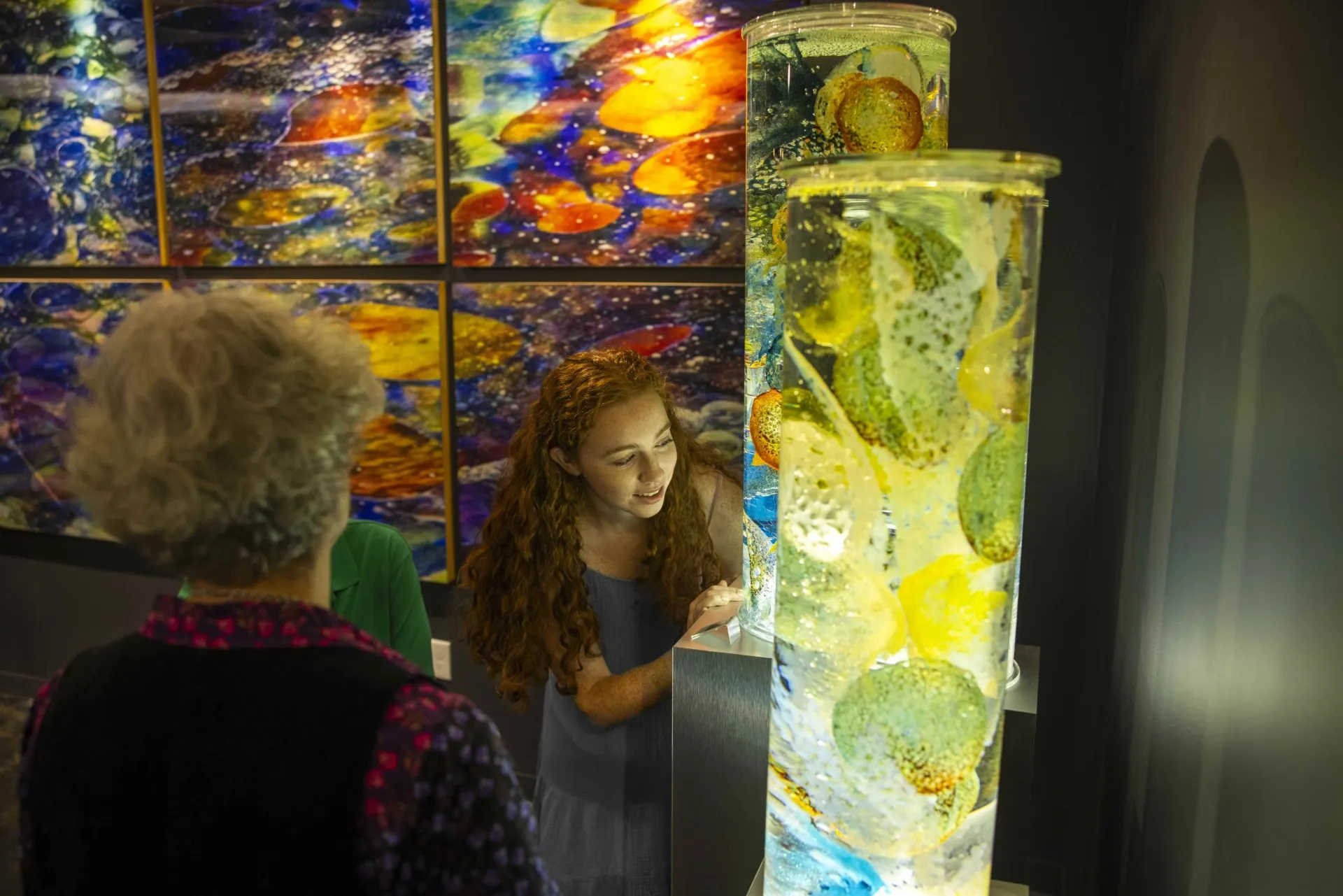 A young girl and an older woman admiring a tall, colorful glass sculpture inside the Torpedo Factory Art Center.