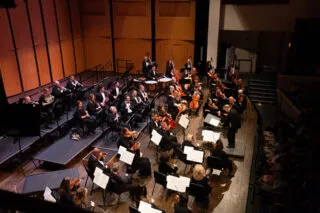 A group of musicians from Alexandria Symphony Orchestra seated on stage with various band instruments.