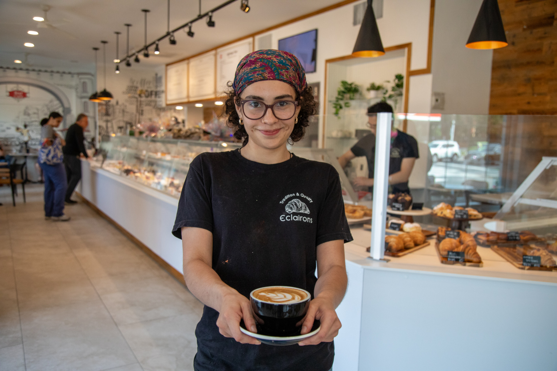 Staff member at Eclairons holding up a cup of coffee.