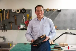 Founder and owner of Old House Provisions, Drew Altizer inside his shoemaking studio and workshop while holding a shoe.