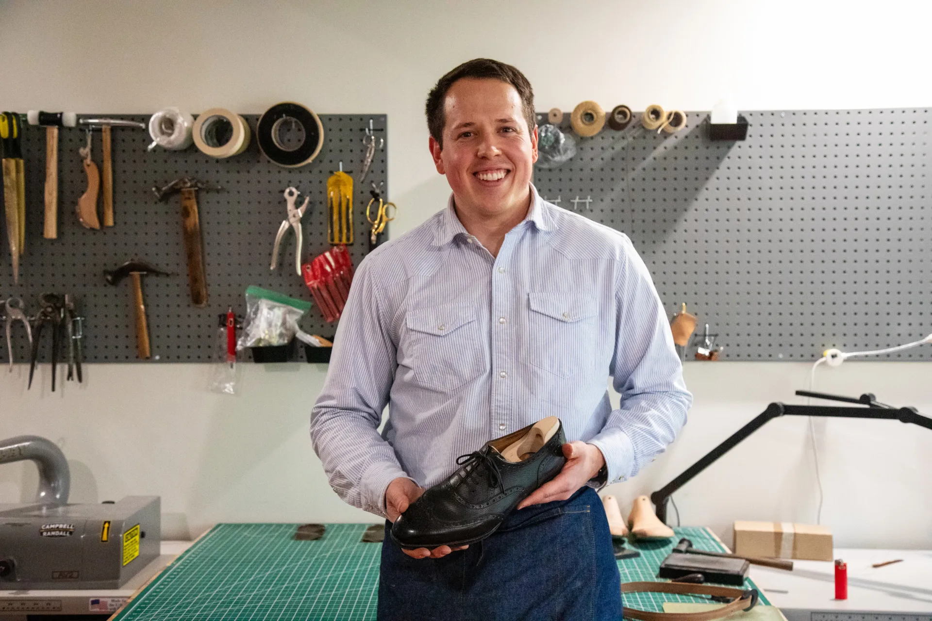 Founder and owner of Old House Provisions, Drew Altizer inside his shoemaking studio and workshop while holding a shoe.