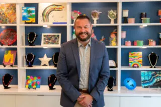Joel Pace standing in front of a display of a wall display of handcrafted artwork.