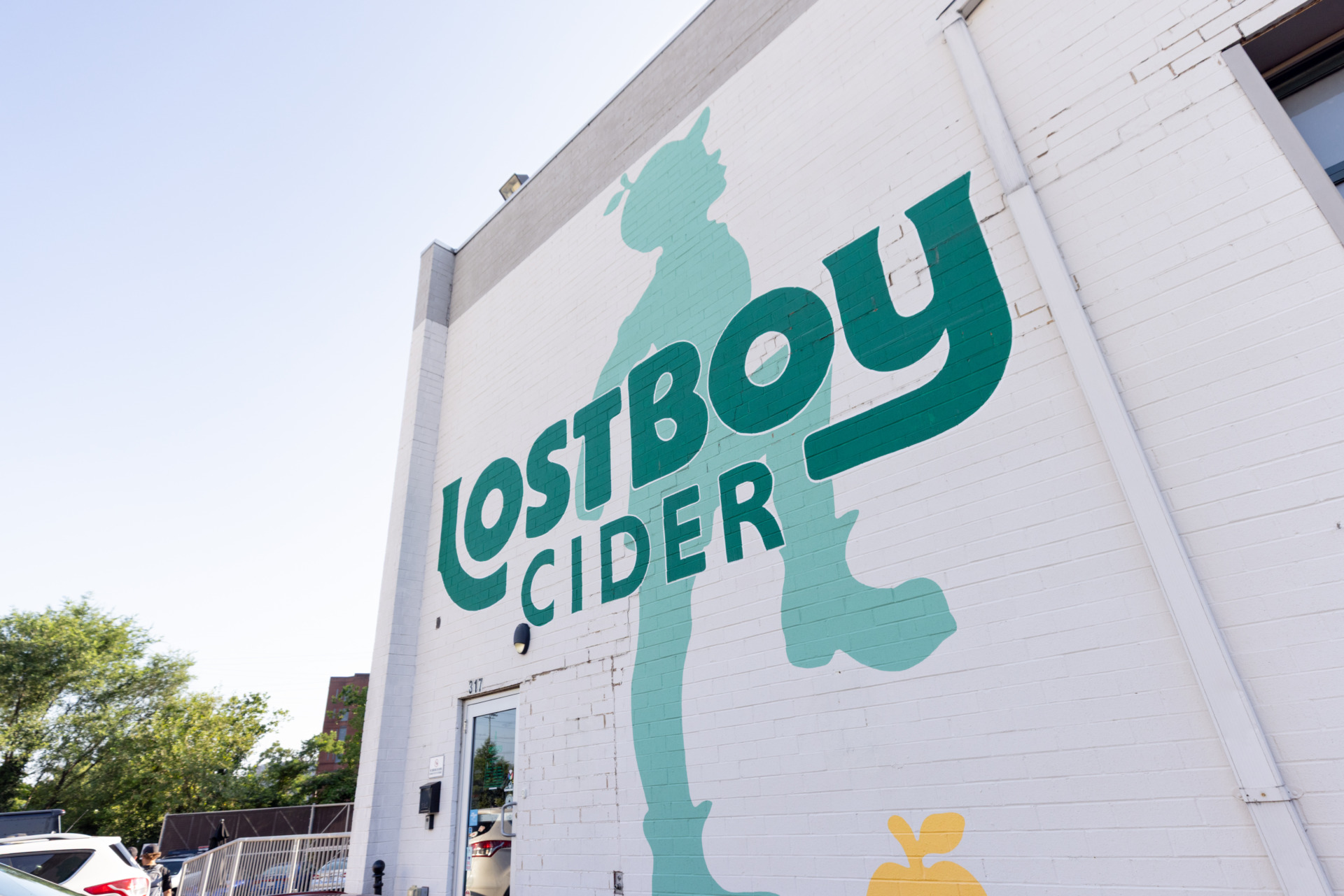 The logo of Lost Boy Cider. A shadow of a boy with an apple on his head and stomping on a yellow apple. The words Lost Boy Cider in front on him.
