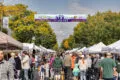 A row of tents lined along Mount Vernon Avenue in Del Ray. Pedestrians are shown walking down the street during Art on the Avenue. The festivals banner is hung above them.