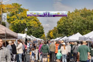 A row of tents lined along Mount Vernon Avenue in Del Ray. Pedestrians are shown walking down the street during Art on the Avenue. The festivals banner is hung above them.