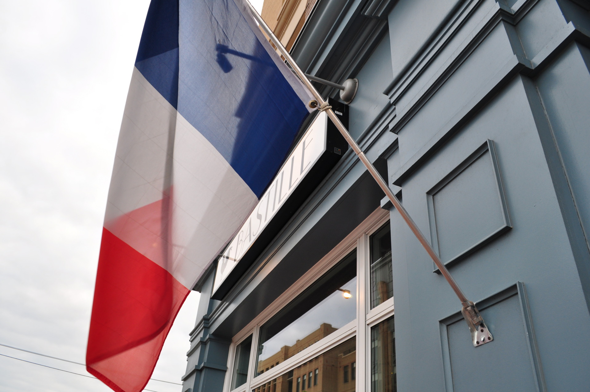 A sign above the entrance of the restaurant, spelling out the word Bastille. France's flag is also show next to the sign.