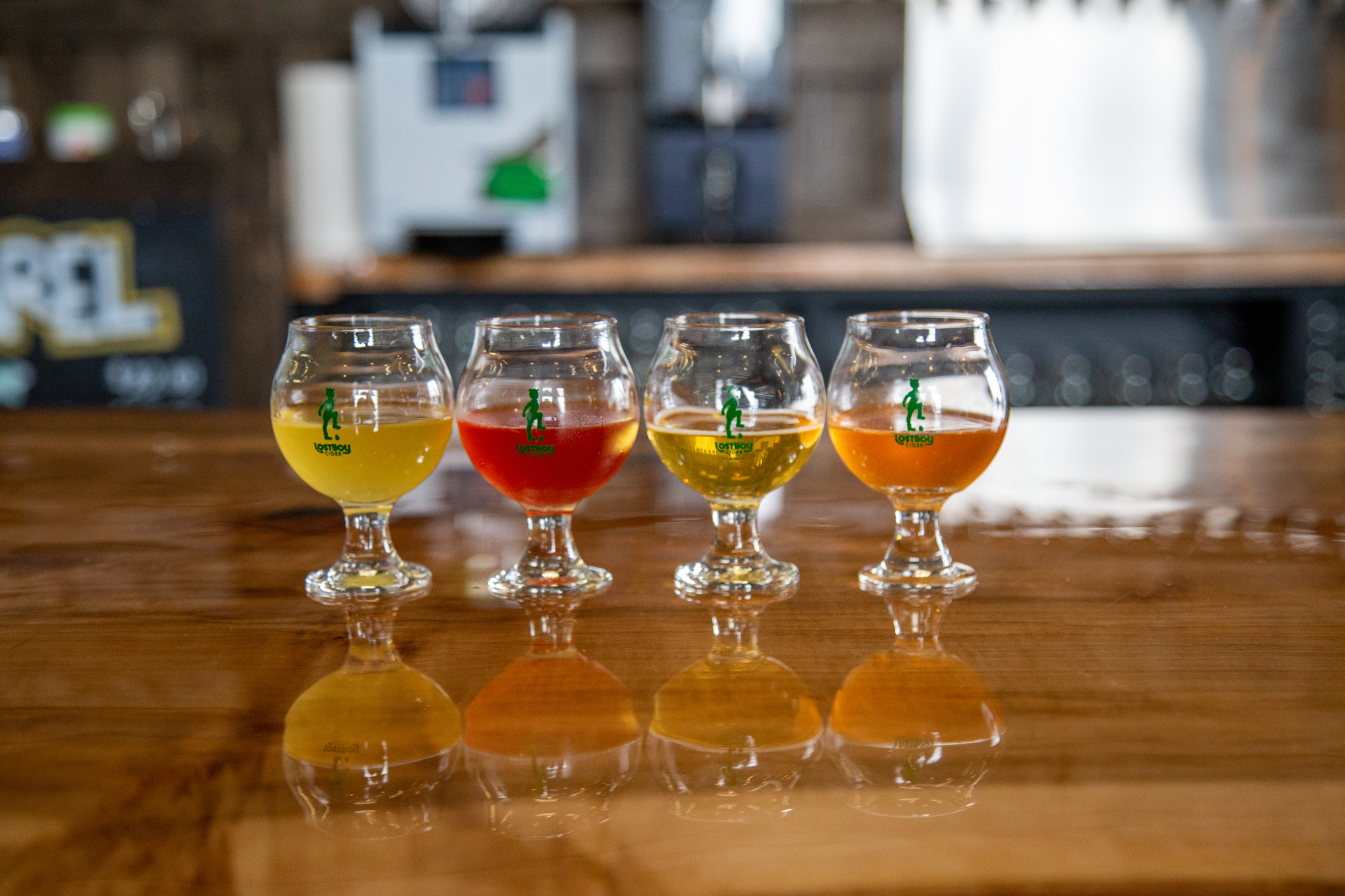 A row of glasses with various colored ciders inside. The Lost Boy Cider logo is on each glass.