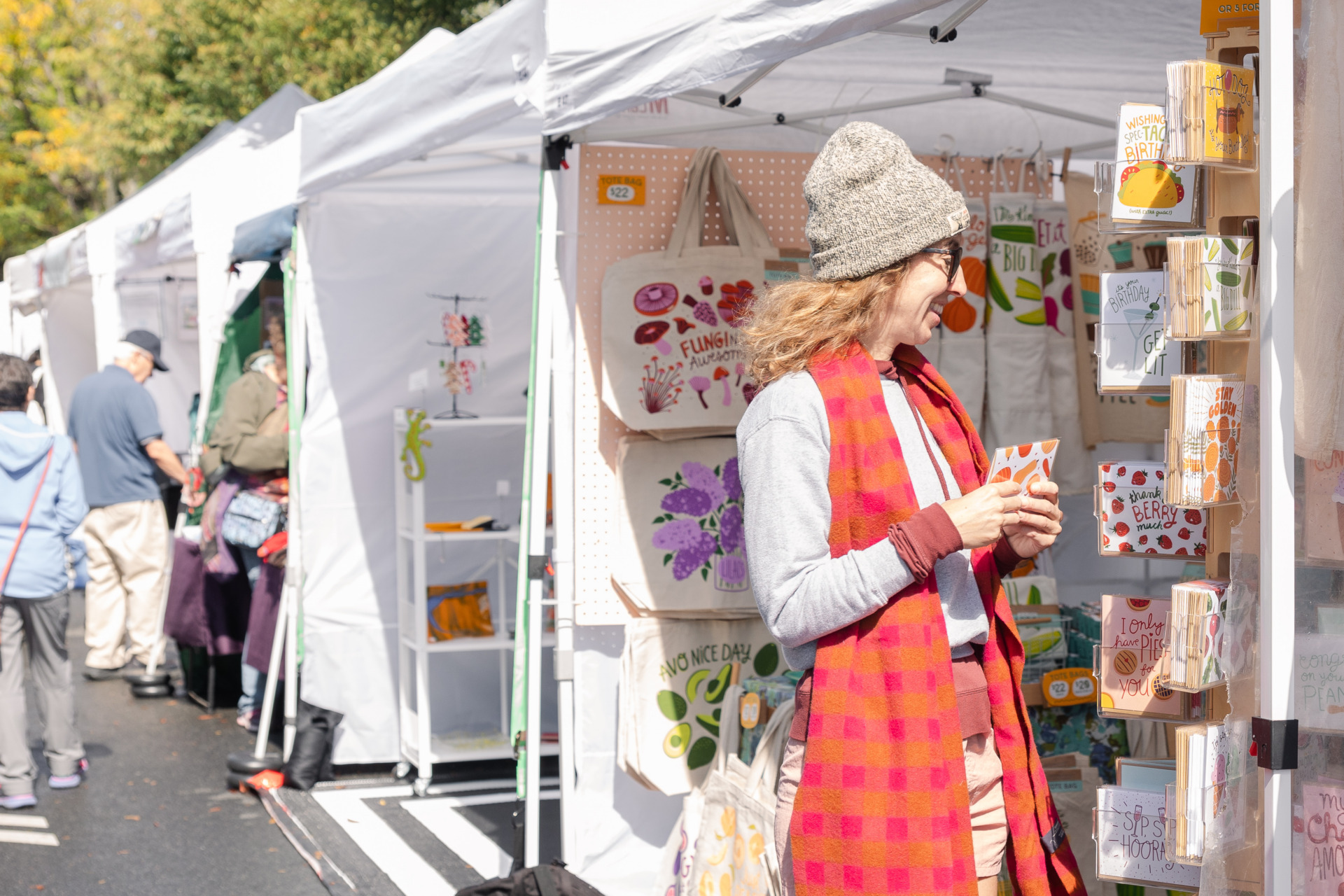 An image of a visitor peeking into an artist's booth selling colorful printed totes and cards. 