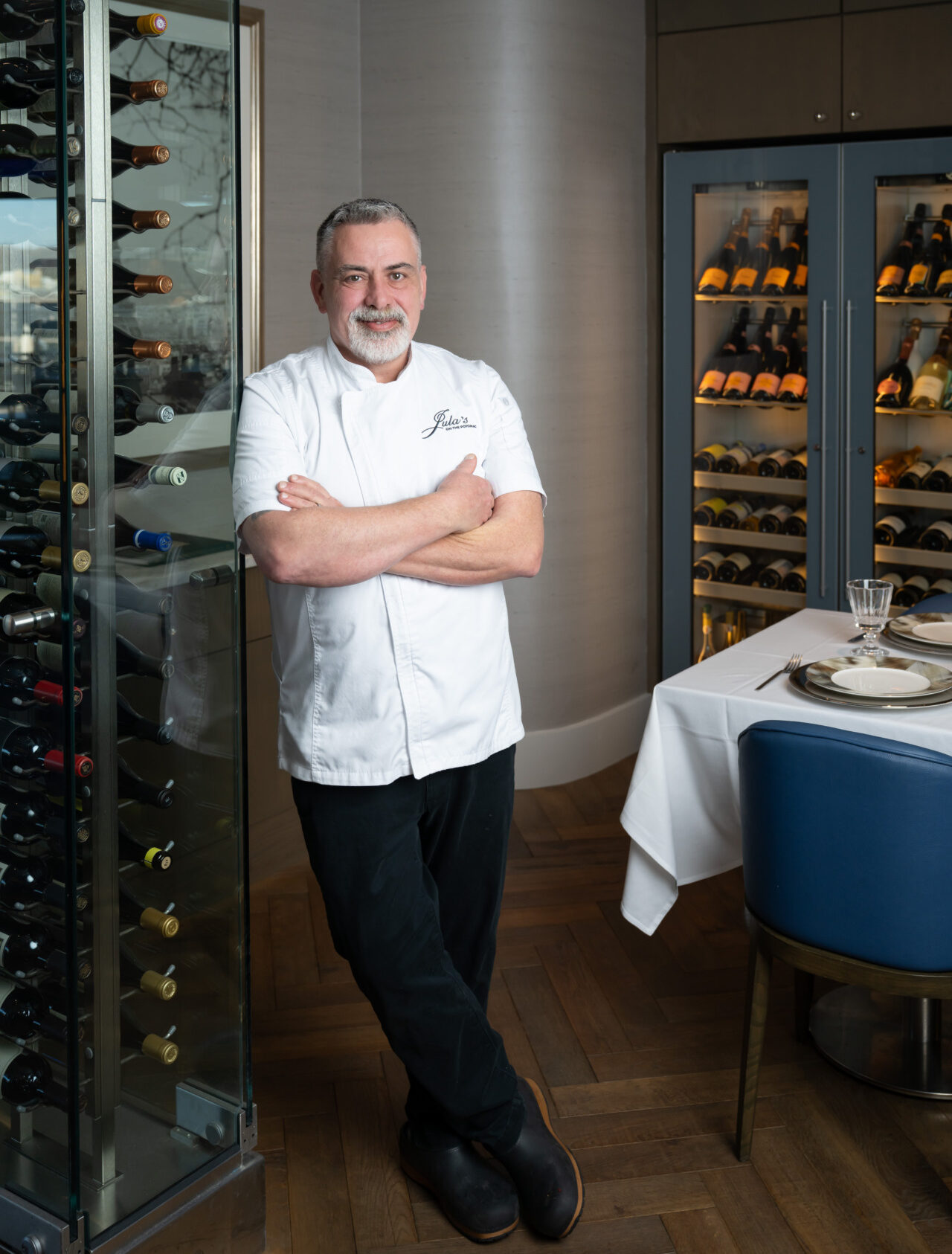 Executive Chef Thomas Crenshaw standing arms crossed against a wine rack.