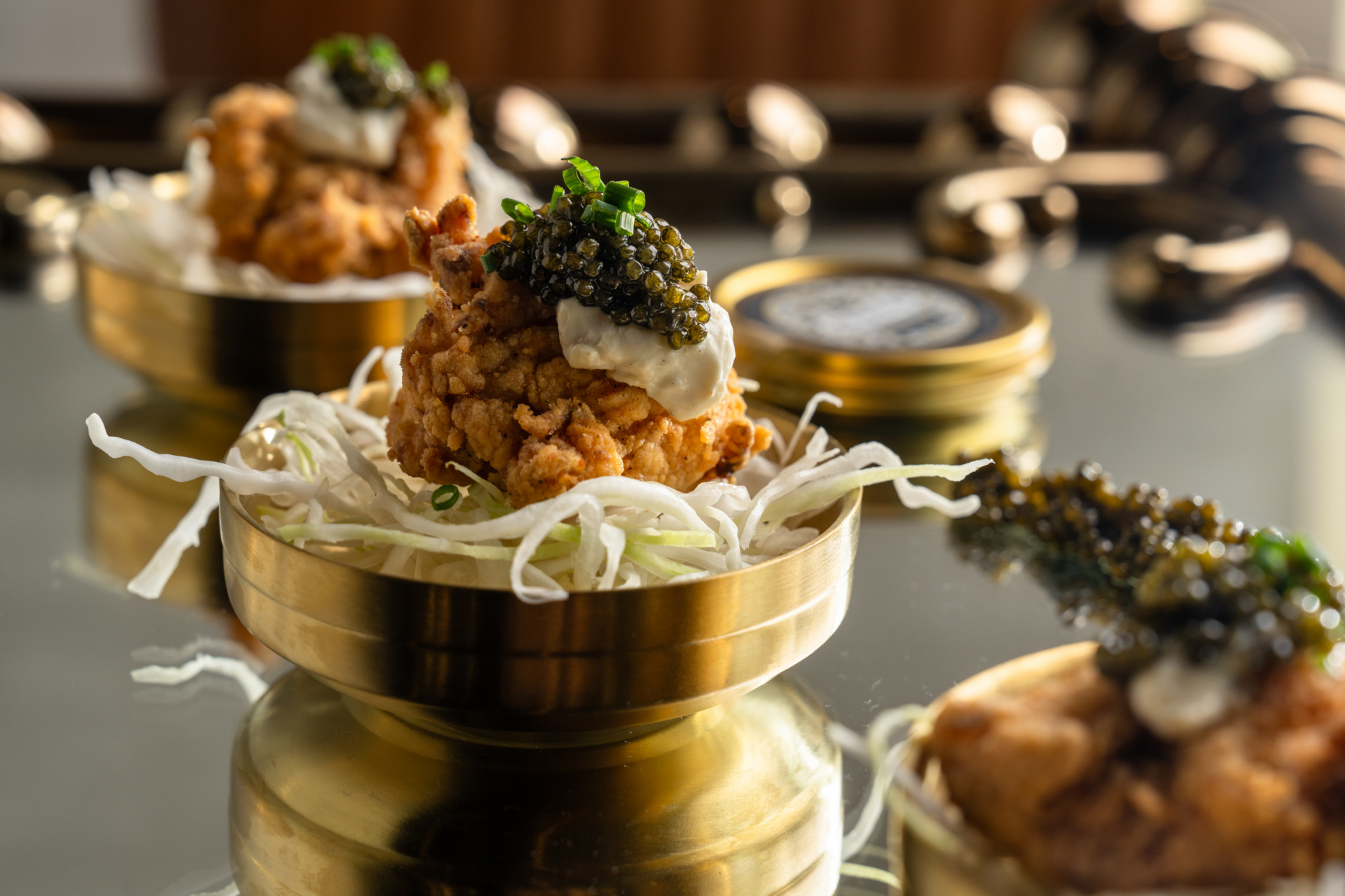 A crispy piece of fried chicken on top of a bed of lettuce and topped with caviar. 