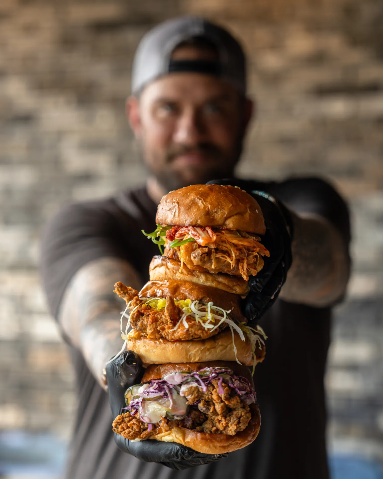 A staff member at Little Birdie holding up three chicken sandwiches stacked on top of the other.