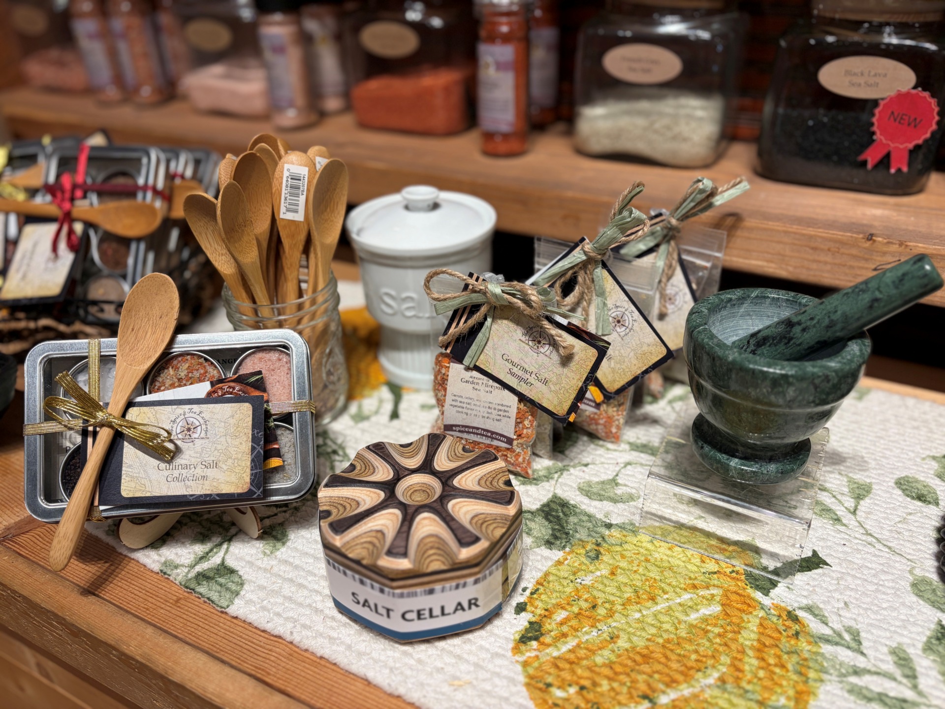 A package of flavored salts, a stone mortar and pedestal, tiny wooden spoons, and more on a display table.